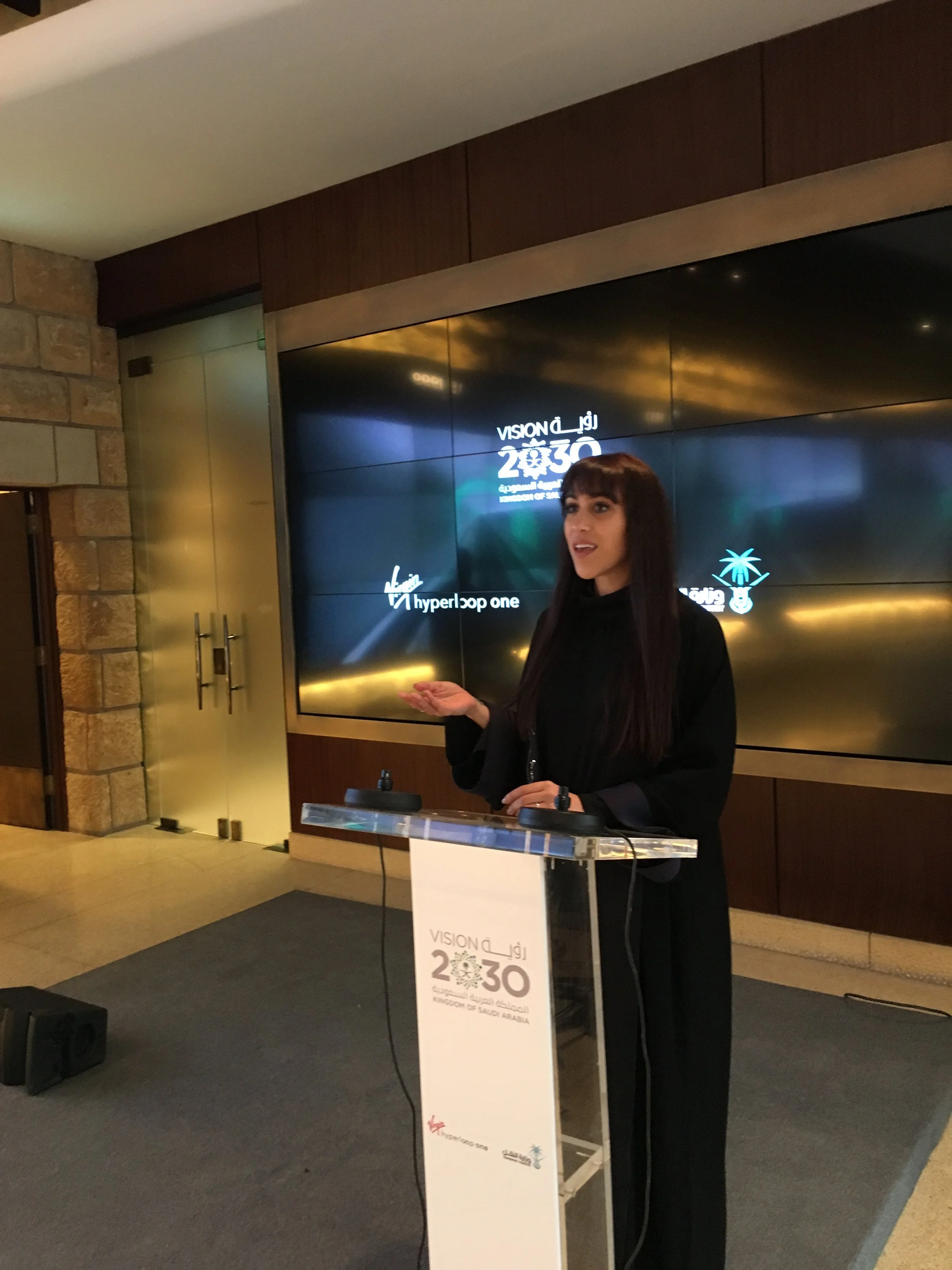 Sarah Iskander presenting before a Vision 2030 screen in Riyadh